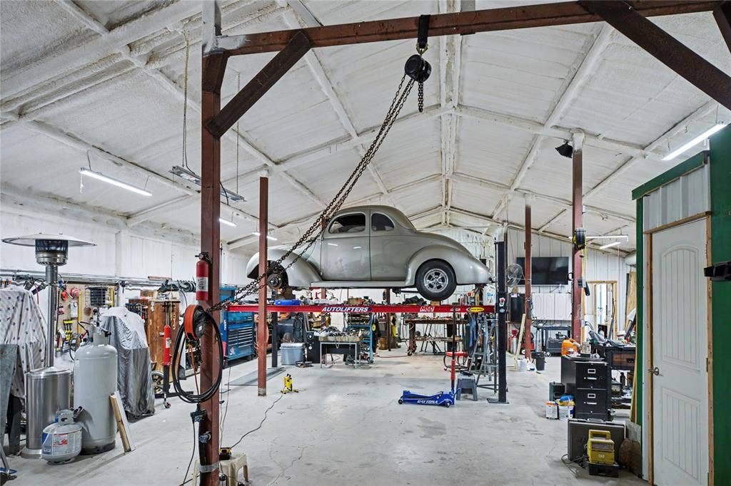 101 Friendship Circle, West Tawakoni, TX 75474 Spacious garage workshop featuring a vehicle lift, vaulted ceiling with exposed beams, fluorescent lighting, and a fire extinguisher