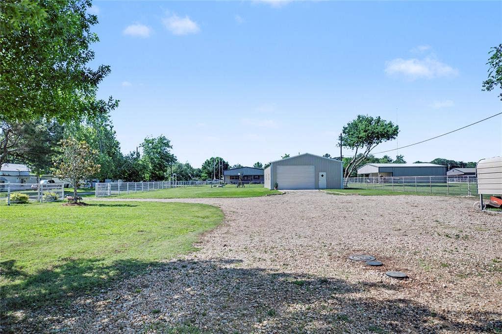 101 Friendship Circle, West Tawakoni, TX 75474 Expansive gravel driveway leading to a metal building featuring a roll-up garage door and an entry door