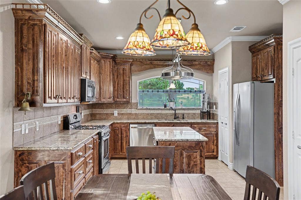 101 Friendship Circle, West Tawakoni, TX 75474 Kitchen featuring extensive wood cabinetry with crown molding, granite countertops, an undermount sink, stainless steel appliances, and tile flooring