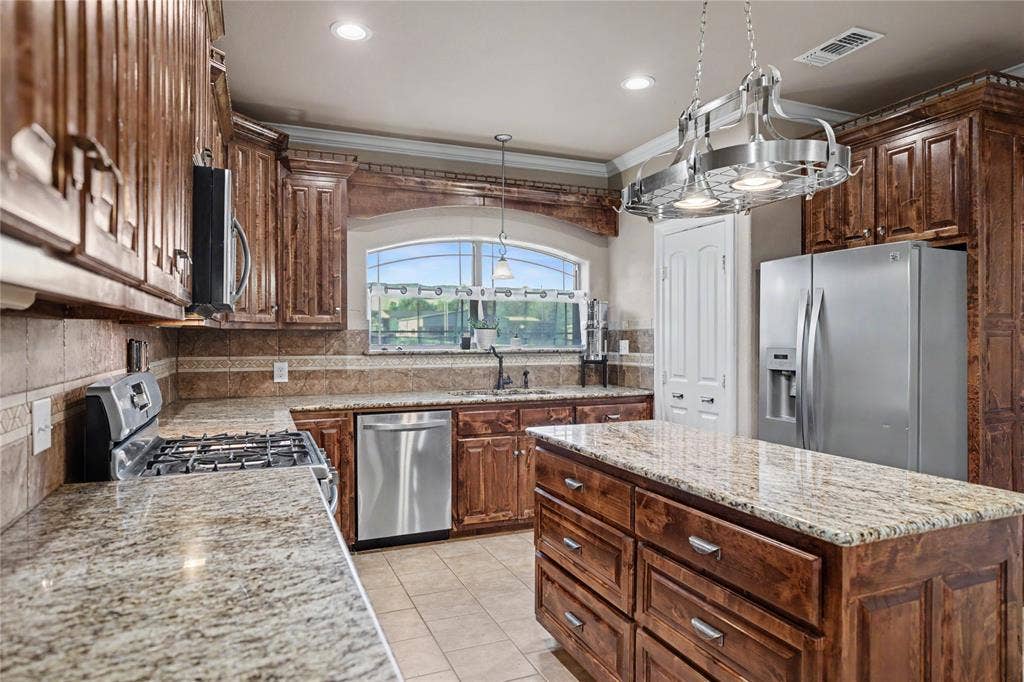 101 Friendship Circle, West Tawakoni, TX 75474 Kitchen featuring a central island with storage, granite countertops, stainless steel appliances, rich wood cabinetry, and a pot rack light fixture