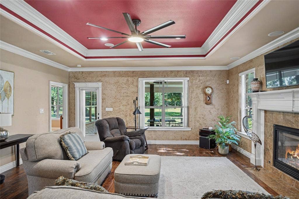 101 Friendship Circle, West Tawakoni, TX 75474 Spacious living area featuring a tray ceiling with a modern ceiling fan, wood-finish flooring, a built-in fireplace with a stone surround, and multiple windows allowing natural light