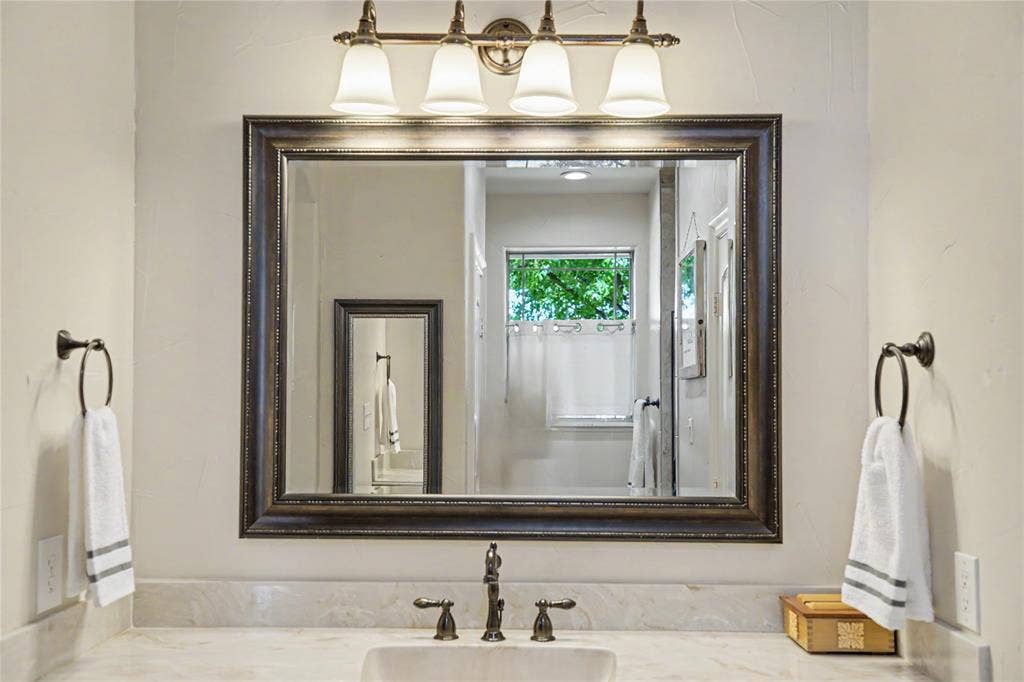 101 Friendship Circle, West Tawakoni, TX 75474 Bathroom vanity featuring a framed mirror, four-light fixture with frosted glass shades, and a bronze-finish faucet