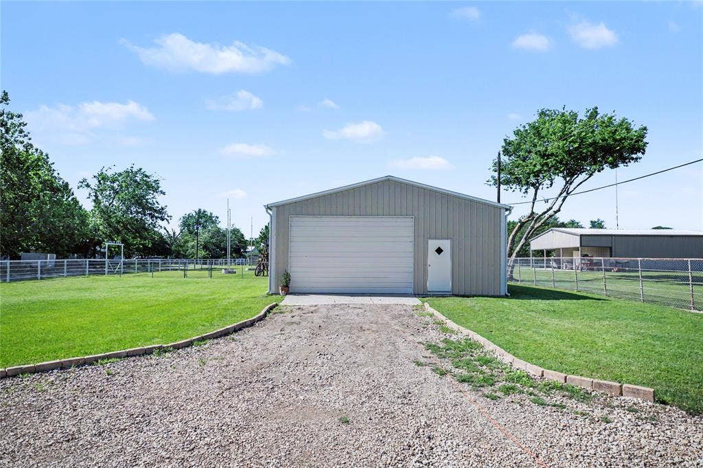 101 Friendship Circle, West Tawakoni, TX 75474 Metal outbuilding featuring a large roll-up door, pedestrian entry, and a gravel driveway with brick edging