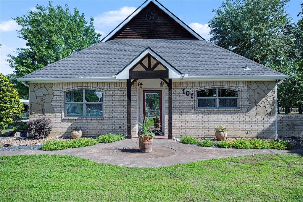 101 Friendship Circle, West Tawakoni, TX 75474 Exterior featuring light brick and stone accents, a gabled roofline with dark wood siding, and a covered entry with exposed timber beams