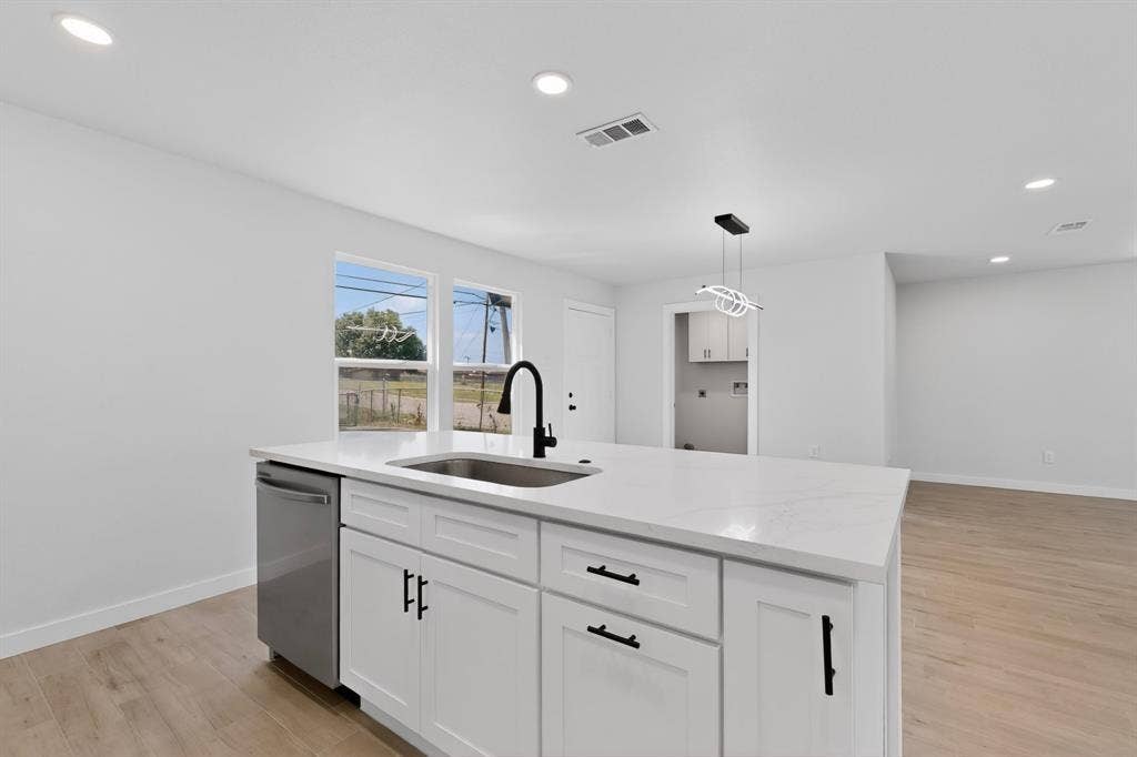 3853 Happy Canyon Drive, Dallas, TX 75241 Kitchen island featuring a stainless steel sink with a black gooseneck faucet, white shaker-style cabinetry with black hardware, and a light-colored countertop