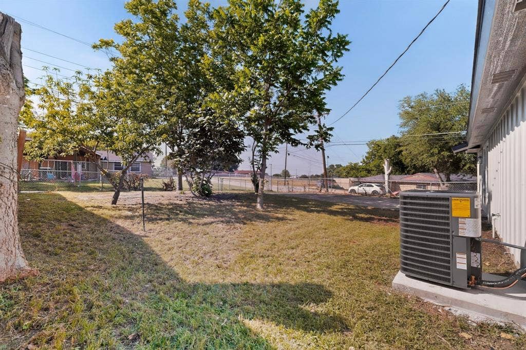 3853 Happy Canyon Drive, Dallas, TX 75241 Expansive grassy area with mature trees and a chain-link fence, featuring an exterior air conditioning unit on a concrete pad
