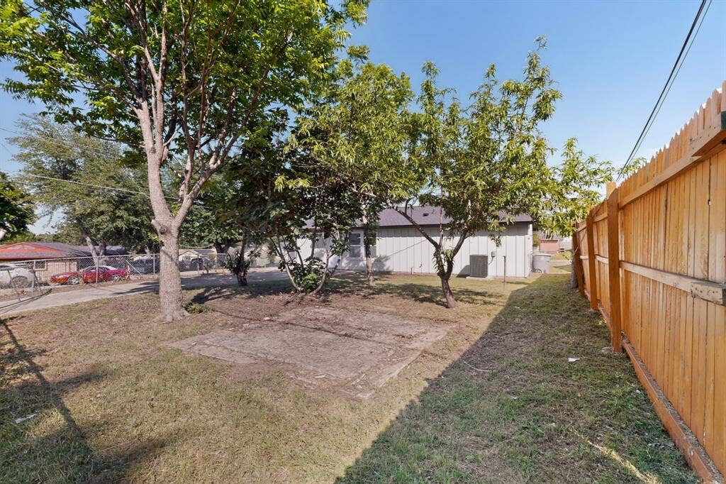 3853 Happy Canyon Drive, Dallas, TX 75241 Expansive grassy yard with mature trees, a privacy fence, and a concrete pad