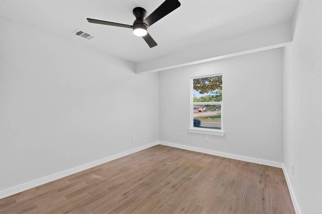 3853 Happy Canyon Drive, Dallas, TX 75241 Spacious room featuring wood-finish flooring, a modern black ceiling fan with integrated lighting, a single window, and crisp white walls