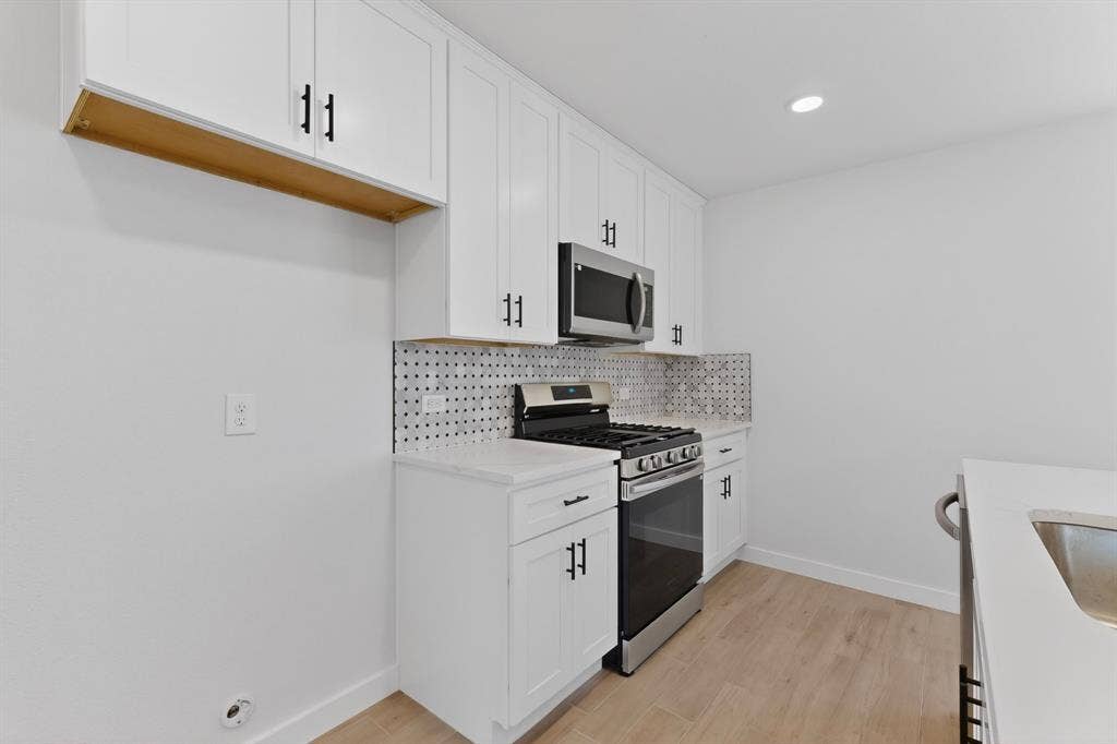 3853 Happy Canyon Drive, Dallas, TX 75241 Kitchen featuring white shaker cabinetry with matte black hardware, stainless steel appliances, patterned tile backsplash, quartz countertops, and wood-finish flooring