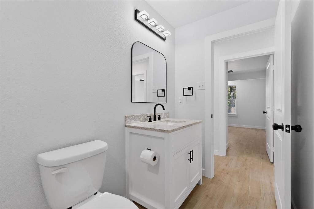 3853 Happy Canyon Drive, Dallas, TX 75241 Bathroom featuring a white vanity with a stone-finish countertop, black hardware, an arched mirror, and a modern light fixture