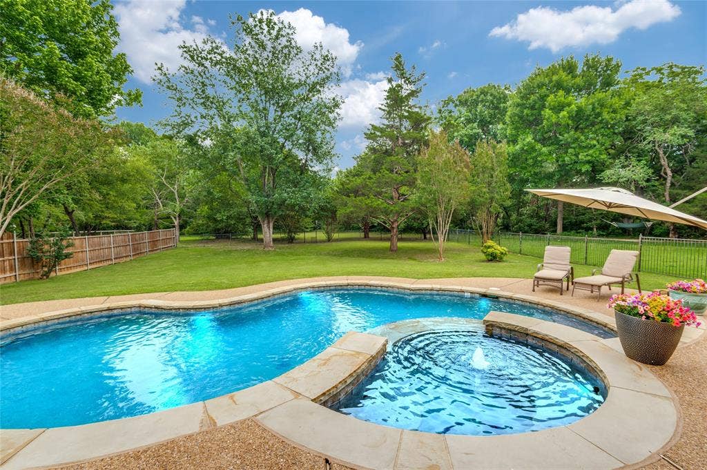108 Appalachian Way, McKinney, TX 75071 Curved swimming pool with integrated spa and fountain feature, surrounded by exposed aggregate concrete decking and stone coping