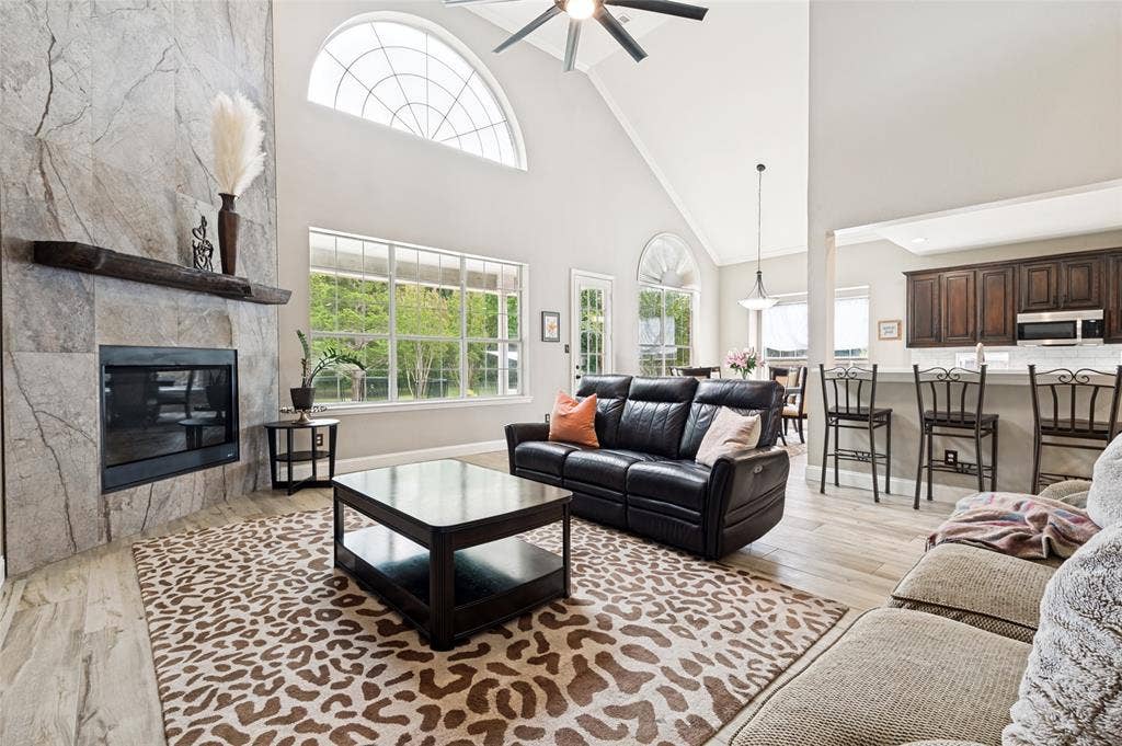 108 Appalachian Way, McKinney, TX 75071 Living area featuring a stone-clad fireplace with a timber mantel, vaulted ceilings, and large windows