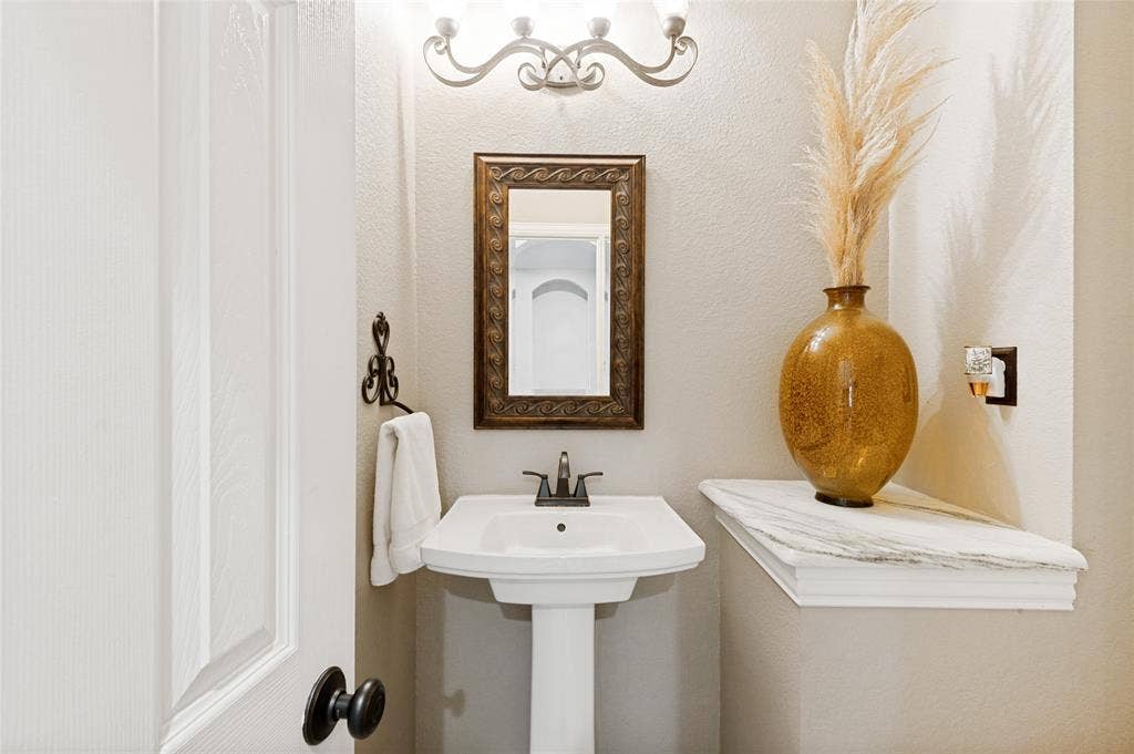 108 Appalachian Way, McKinney, TX 75071 Pedestal sink with black faucet, framed mirror, and wall-mounted vanity lighting