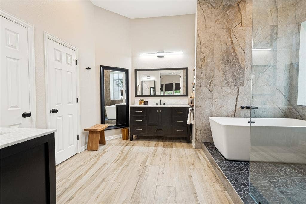 108 Appalachian Way, McKinney, TX 75071 Contemporary bathroom featuring a freestanding tub, a walk-in shower with a glass enclosure, a dark wood-finish vanity with a double sink, and wood-look tile flooring