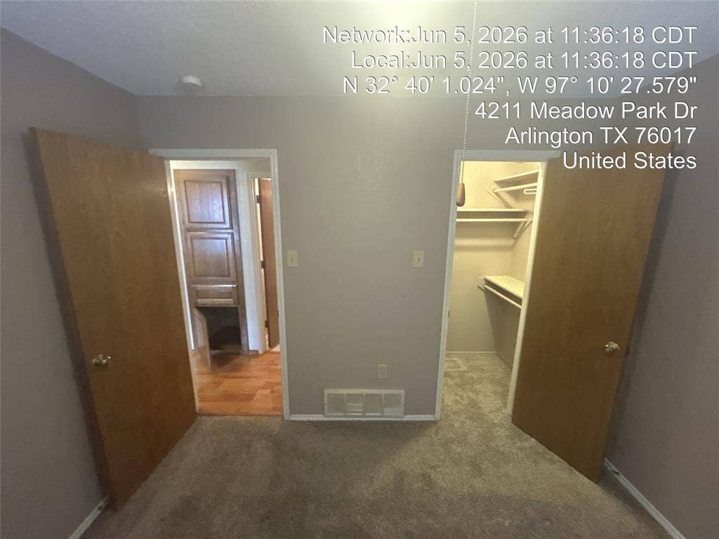 4211 Meadow Park Drive, Arlington, TX 76017 Carpeted room featuring a light gray wall color, two wood-finish doors, a closet with shelving, and a doorway leading to a space with wood-finish flooring and built-in cabinetry