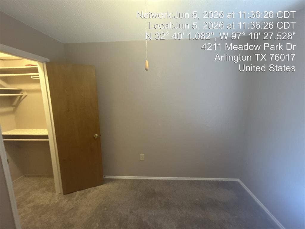 4211 Meadow Park Drive, Arlington, TX 76017 Spacious interior room featuring light gray wall paint, gray carpeting, a light wood-finish door, and a walk-in closet with built-in shelving