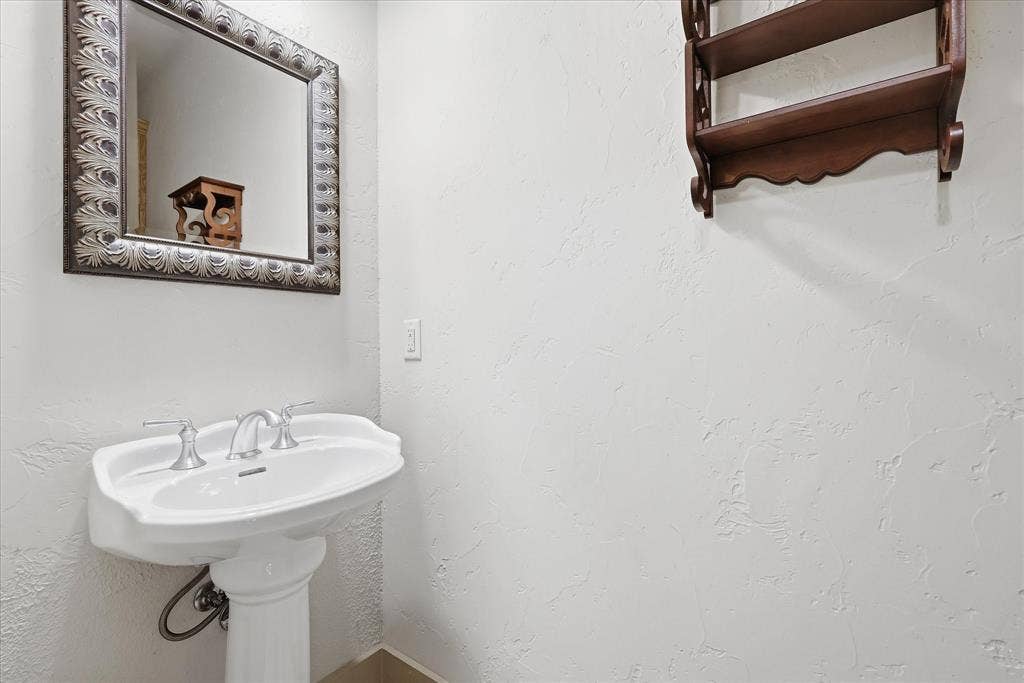 413 Collins Street, Argyle, TX 76226 Pedestal sink with dual-handle chrome faucet, complemented by a framed mirror with an ornate surround