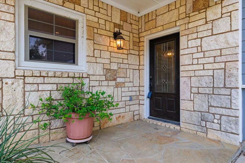 413 Collins Street, Argyle, TX 76226 Stone veneer facade featuring a dark entry door with decorative glass, a white-framed window, and a wall-mounted sconce