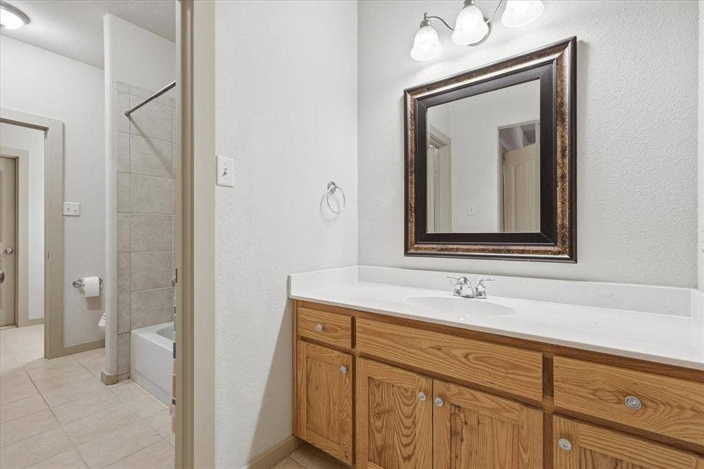 413 Collins Street, Argyle, TX 76226 Bathroom featuring a wood-finish vanity with a white countertop, an undermount sink, a framed mirror, and a three-light fixture