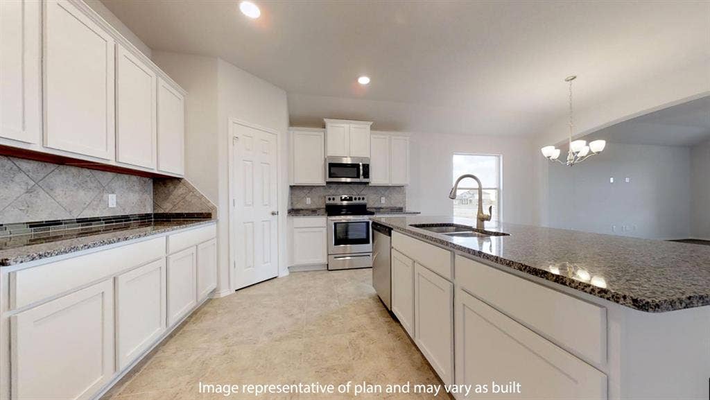 Modern kitchen featuring white cabinetry, stone countertops, stainless steel appliances, a tiled backsplash, and an island with an integrated sink