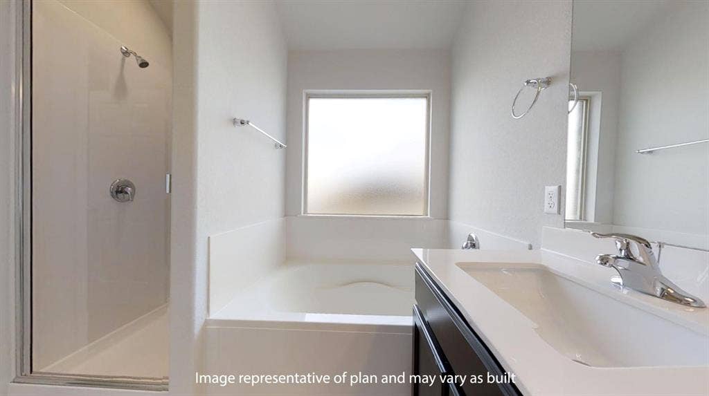 Bathroom featuring a built-in tub with a frosted window, separate shower enclosure with chrome fixtures, a vanity with an integrated sink, and a framed mirror