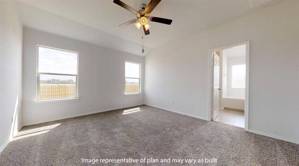 Spacious room featuring neutral carpeting, a ceiling fan with integrated lighting, two windows with white trim, and a doorway leading to a tiled bathroom with a tub