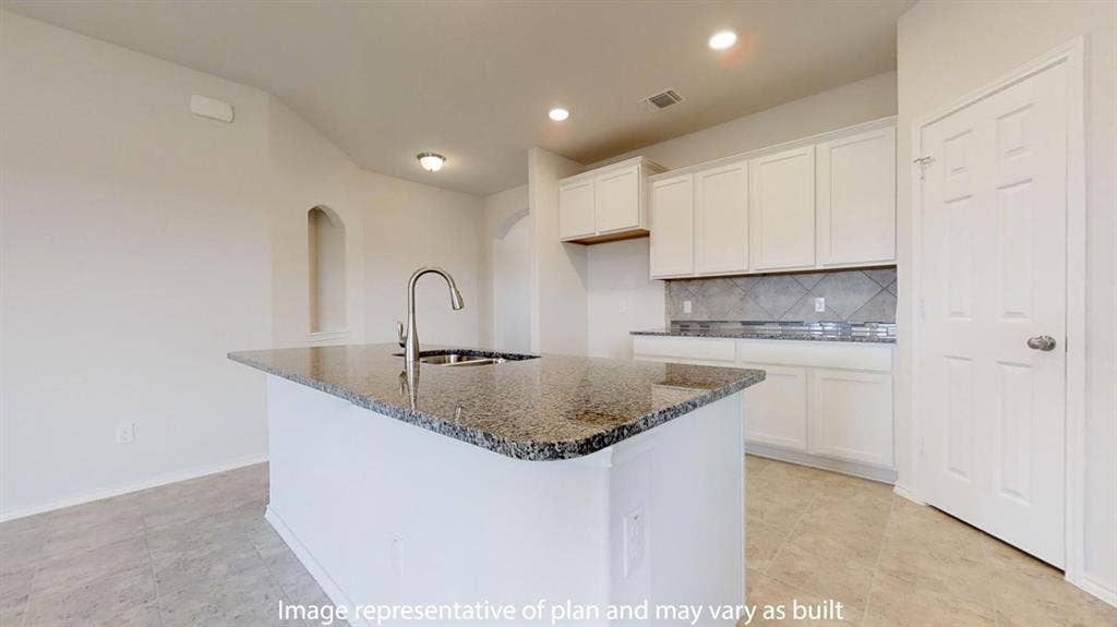 Kitchen island featuring a stainless steel sink with a high-arc faucet, granite countertop, white cabinetry, tile backsplash, and recessed lighting