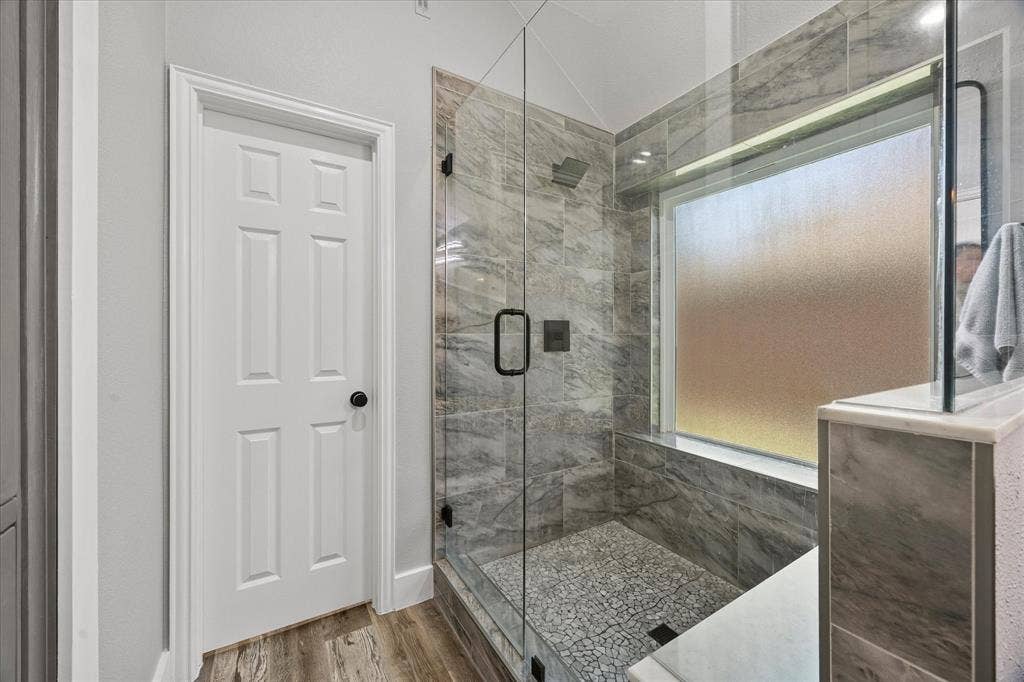 The newly renovated oversized shower includes a frameless glass enclosure, tiled surround, bench seat and pebble tile floor.
