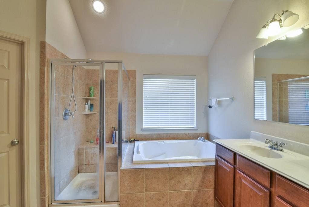 2705 Fox Creek Trail, Arlington, TX 76017 Bathroom featuring a built-in tub with tile surround, a separate glass-enclosed shower with tile walls and integrated shelving, a wood-finish vanity with a single sink and light-toned countertop, and recessed ceiling lighting