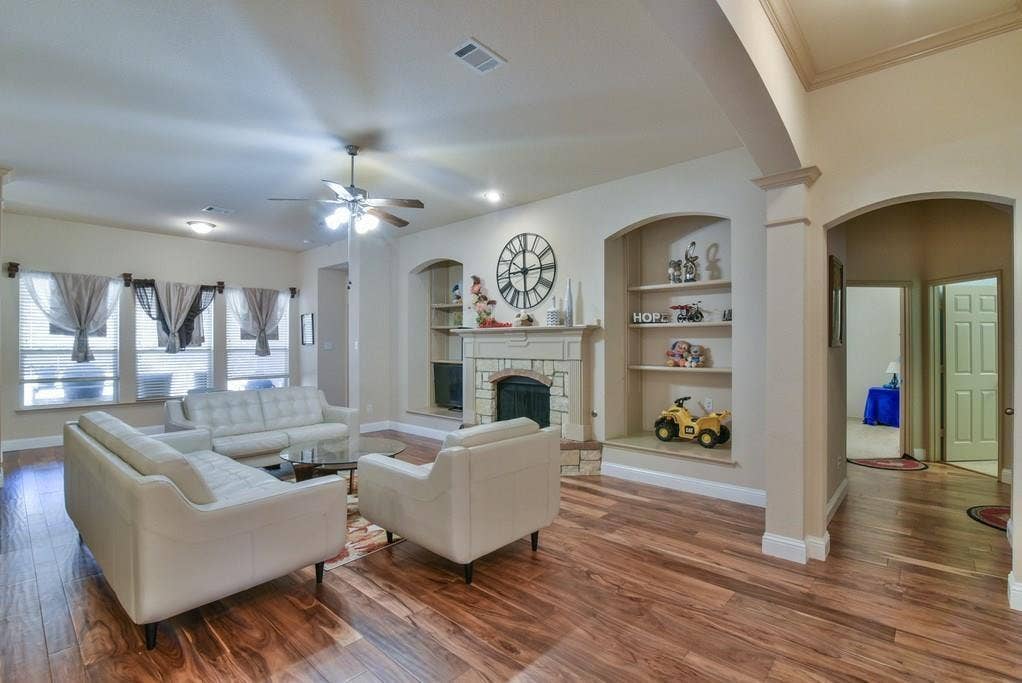 2705 Fox Creek Trail, Arlington, TX 76017 Spacious living area featuring wood-finish flooring, a stone-surround fireplace, built-in shelving, arched doorways, and a ceiling fan
