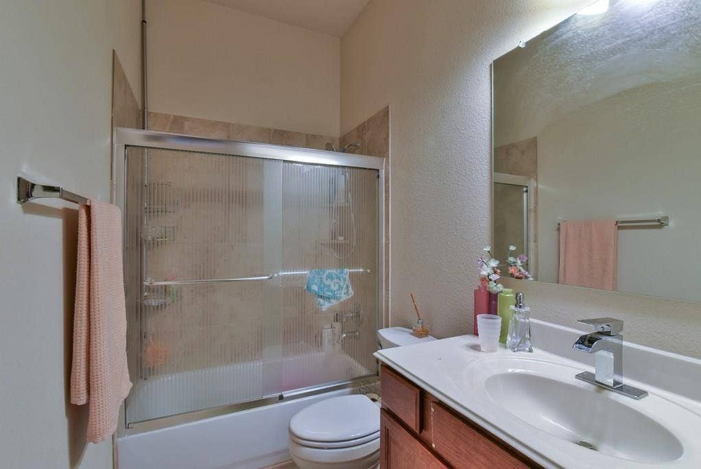 2705 Fox Creek Trail, Arlington, TX 76017 Bathroom featuring a wood-finish vanity with an integrated sink and chrome faucet, a large wall-mounted mirror, and a bathtub with a textured glass sliding door