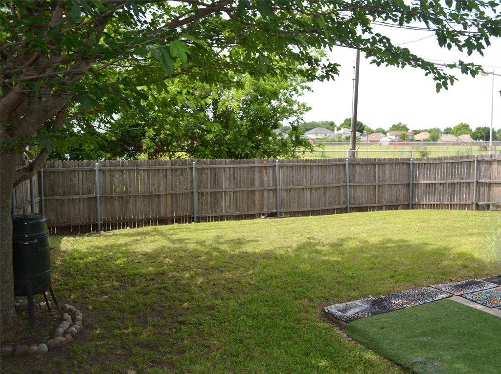 9615 Sophora Circle, Dallas, TX 75249 Expansive backyard featuring a wood privacy fence, mature shade tree, and a grass lawn