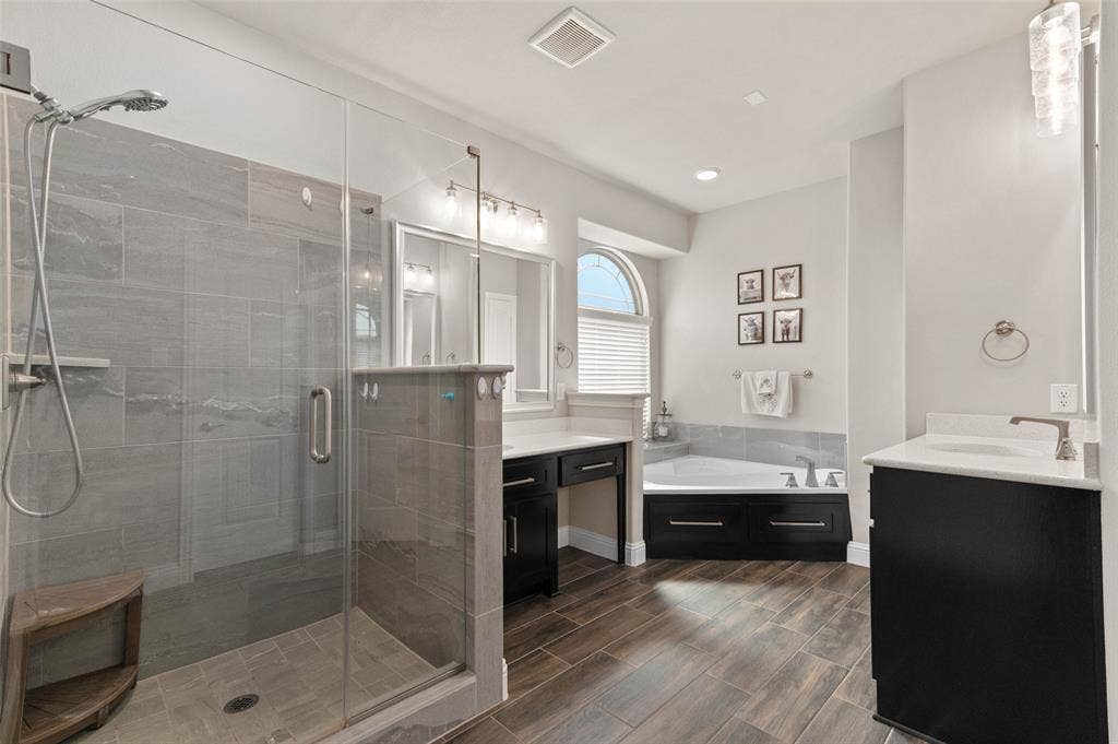 800 Beckington Drive, Shady Shores, TX 76208 Spacious Primary bathroom featuring a glass-enclosed shower with large format tile, wood-finish flooring, a soaking tub with tile surround, and dual vanity areas with dark cabinetry