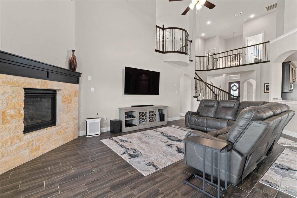 800 Beckington Drive, Shady Shores, TX 76208 Two-story living area featuring a stone fireplace with a dark wood mantle, wood-look tile flooring, and a decorative wrought iron staircase and balcony