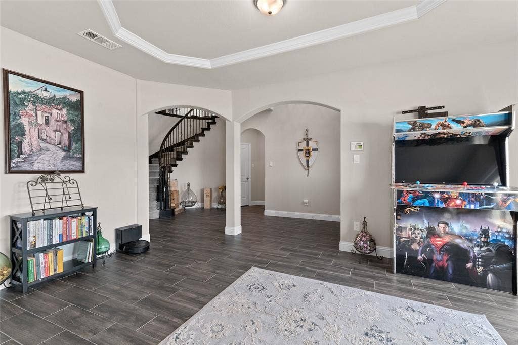 800 Beckington Drive, Shady Shores, TX 76208 Expansive open-concept living space featuring wood-finish flooring, arched doorways, a tray ceiling with crown molding, and a prominent curved staircase with dark wood handrails and wrought iron balusters