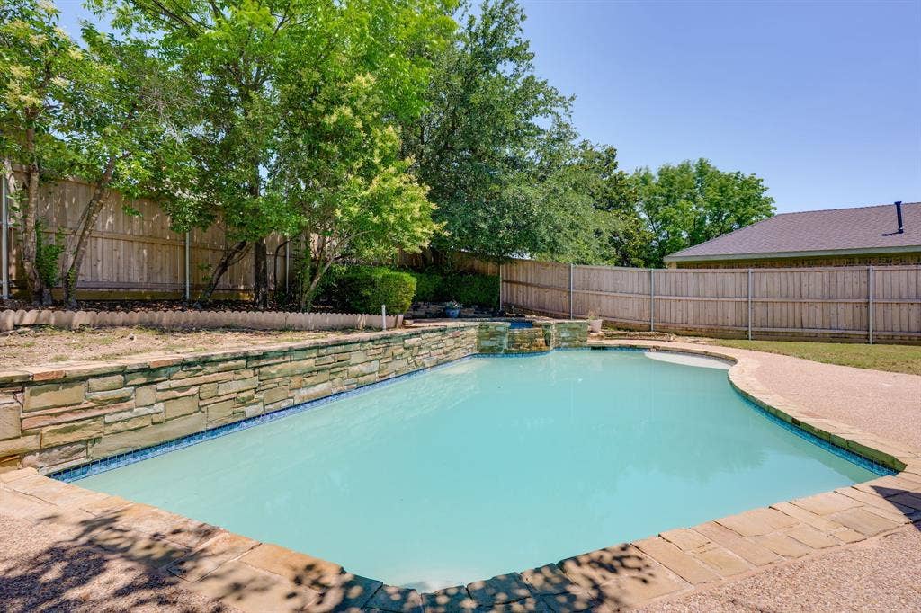 3406 Windridge Drive, Garland, TX 75043 Freeform swimming pool featuring a stone-clad raised spa with waterfall, flagstone coping, and exposed aggregate decking