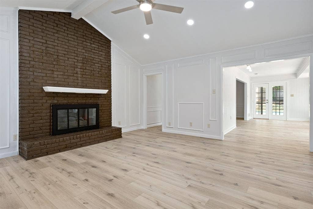 3406 Windridge Drive, Garland, TX 75043 Spacious living area featuring a prominent brick fireplace with a white mantel, vaulted ceilings with exposed beams, recessed lighting, and wood-finish flooring