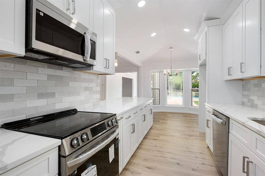 3406 Windridge Drive, Garland, TX 75043 Updated kitchen featuring white shaker cabinetry, stainless steel appliances, light-toned wood-finish flooring, and a subway tile backsplash