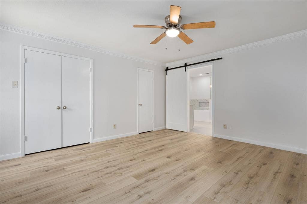 3406 Windridge Drive, Garland, TX 75043 Spacious room featuring wood-finish flooring, ceiling fan with light fixture, crown molding, and a barn door leading to an adjoining area