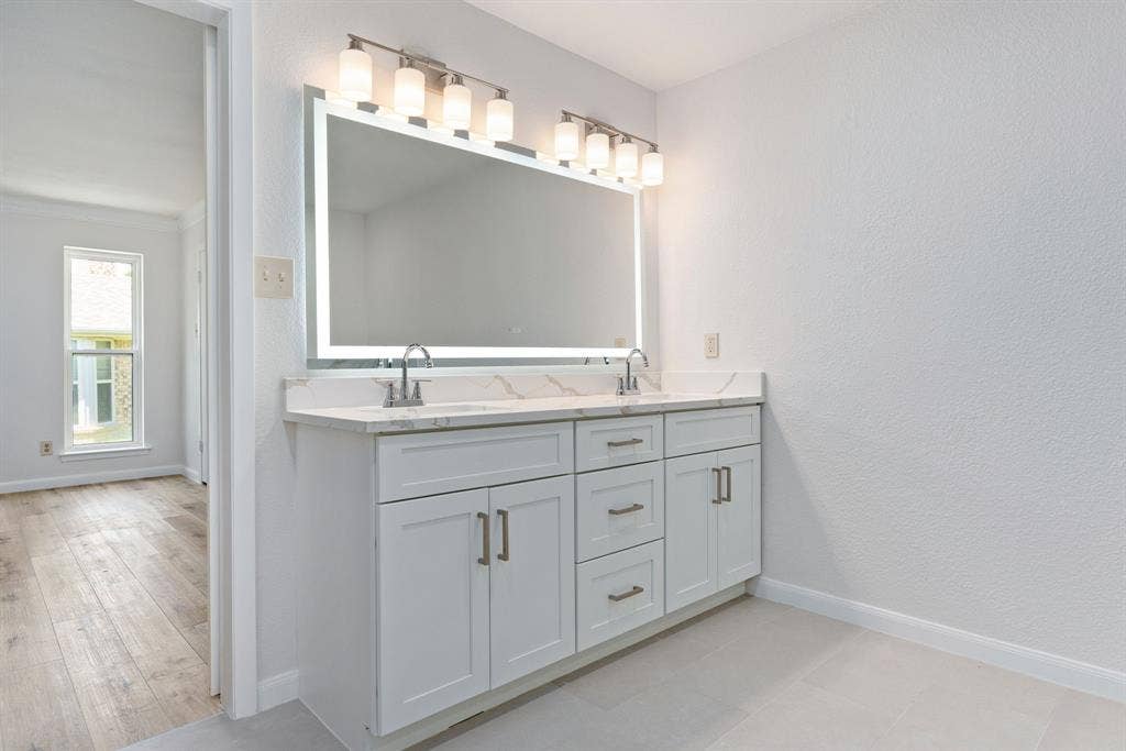 3406 Windridge Drive, Garland, TX 75043 Dual vanity featuring white shaker cabinetry, brushed nickel hardware, and a stone-finish countertop