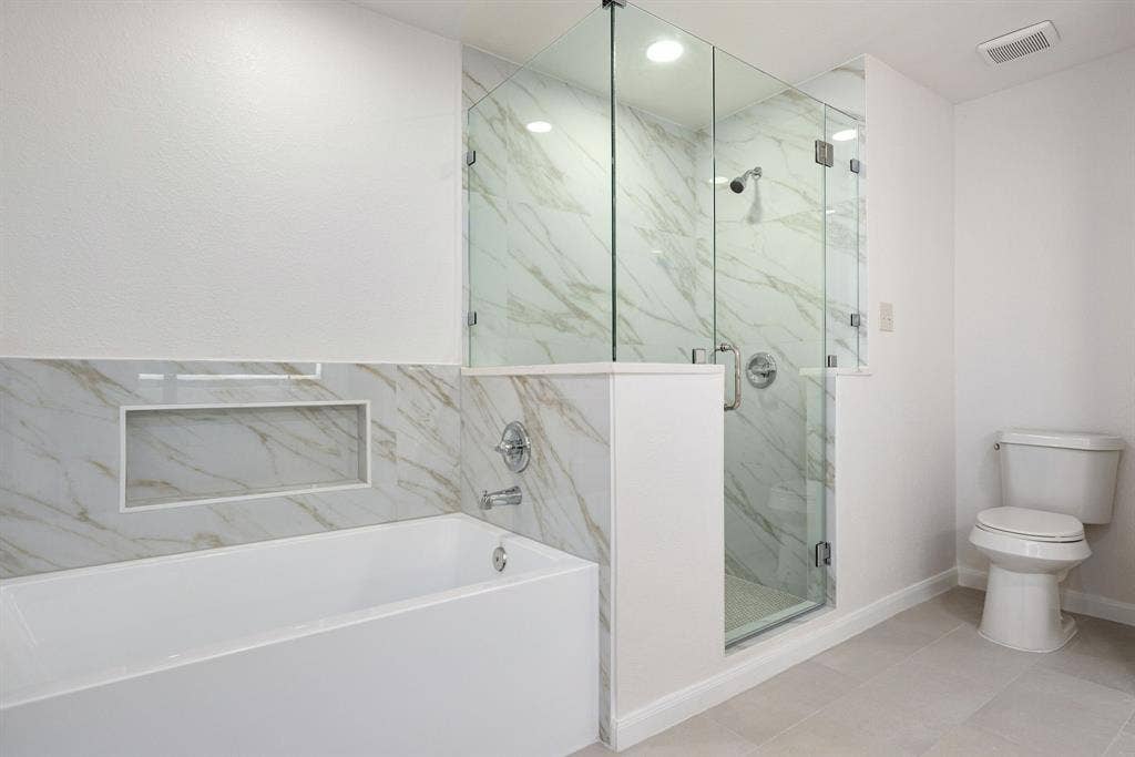 3406 Windridge Drive, Garland, TX 75043 Contemporary bathroom featuring a freestanding tub, glass-enclosed shower, white marble-look wall tiling, recessed shower lighting, and light-toned floor tiling