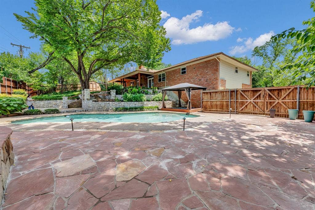 3908 Wildwood, Euless, TX 76040 Expansive flagstone patio with a swimming pool, stone retaining walls, and a wooden privacy fence