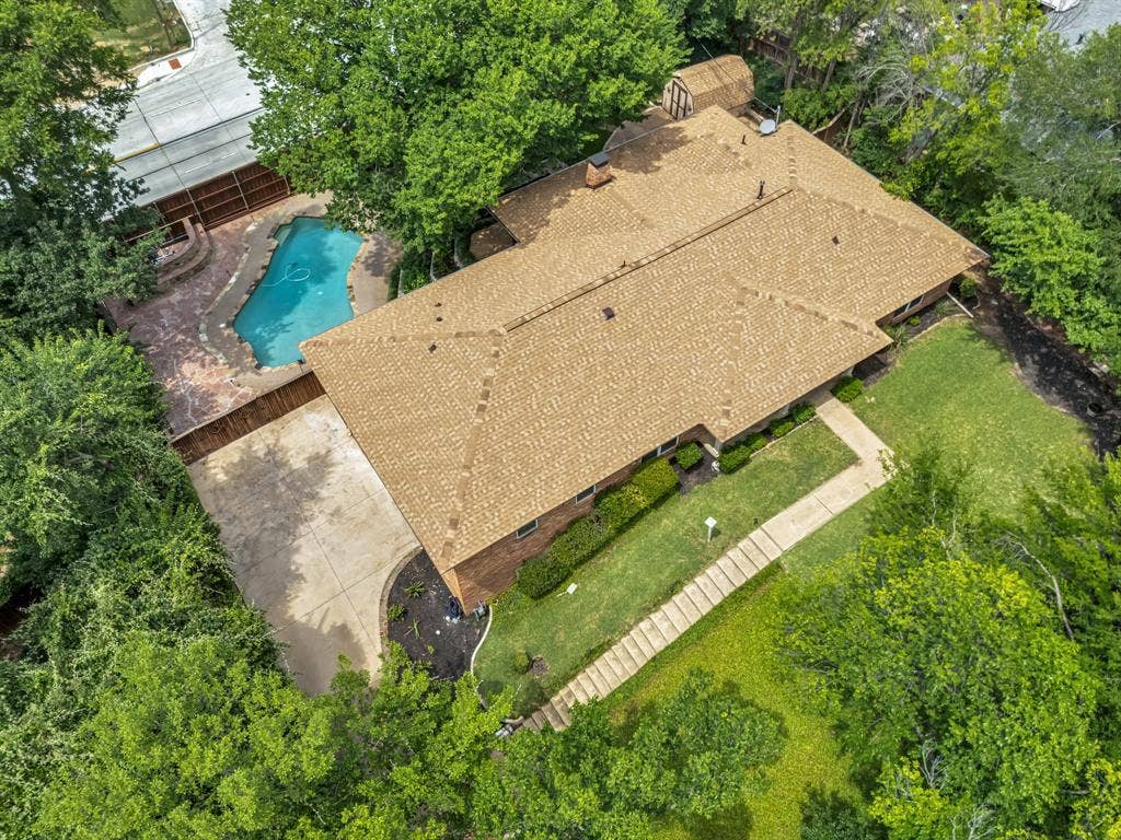 3908 Wildwood, Euless, TX 76040 Aerial view showcasing a residential property with a shingle roof, a swimming pool with a stone-finish patio, a concrete driveway, a sidewalk leading to the entrance, and surrounding mature trees