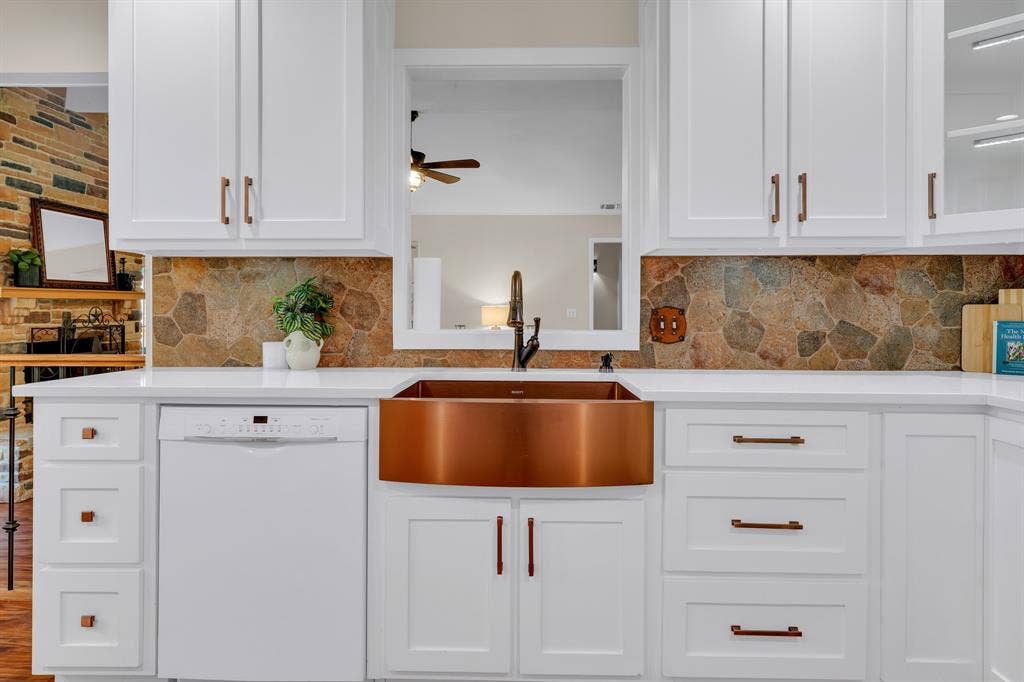 3908 Wildwood, Euless, TX 76040 Kitchen featuring white cabinetry with bronze-finish hardware, a copper farmhouse sink with a dark bronze faucet, a stone backsplash, and white countertops