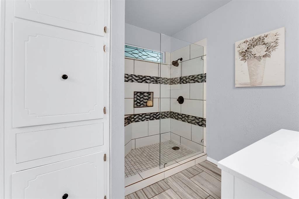 3908 Wildwood, Euless, TX 76040 Walk-in shower with clear glass enclosure, white subway tile surround, mosaic accent stripe, and built-in shelving