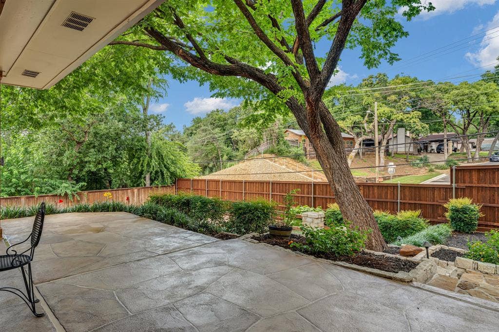 3908 Wildwood, Euless, TX 76040 Covered patio with stamped concrete flooring, surrounded by lush landscaping and a mature tree
