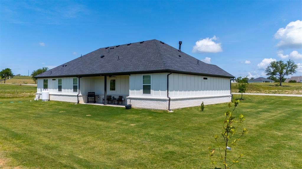 2004 Willy Dilly Road, Springtown, TX 76082 Expansive rear exterior featuring a covered patio, a manicured lawn, white vertical siding, and a dark shingle roof
