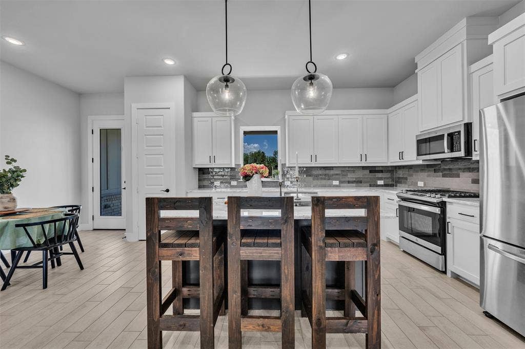2004 Willy Dilly Road, Springtown, TX 76082 Modern kitchen featuring white shaker cabinetry, stainless steel appliances, a large center island with a stone countertop, a tile backsplash, and wood-finish flooring