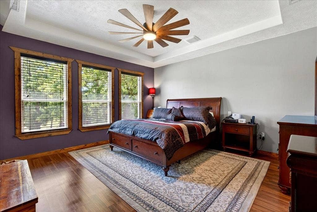 11591 Farm Market 59, Athens, TX 75751 Primary bedroom featuring wood-finish flooring, a tray ceiling, and a farm style ceiling fan with integrated lighting, pretty outdoor view from the windows.