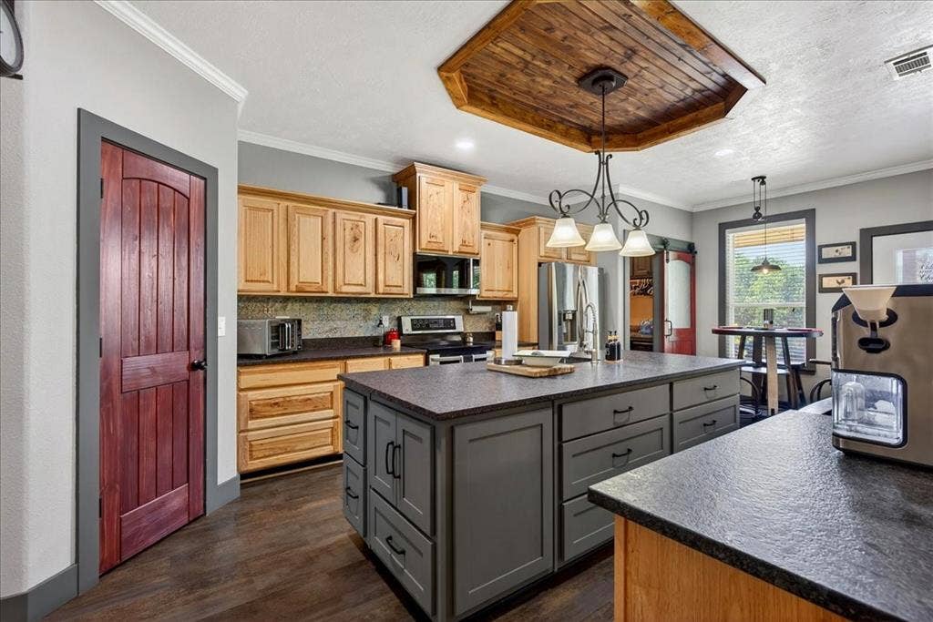 11591 Farm Market 59, Athens, TX 75751 Kitchen featuring a central island with integrated storage, wood-finish flooring, light wood cabinetry, stone-look countertops, and a wood-paneled ceiling accents, granite counters, pine cabinets, tile back splash, double black metal farm sink, large pantry.